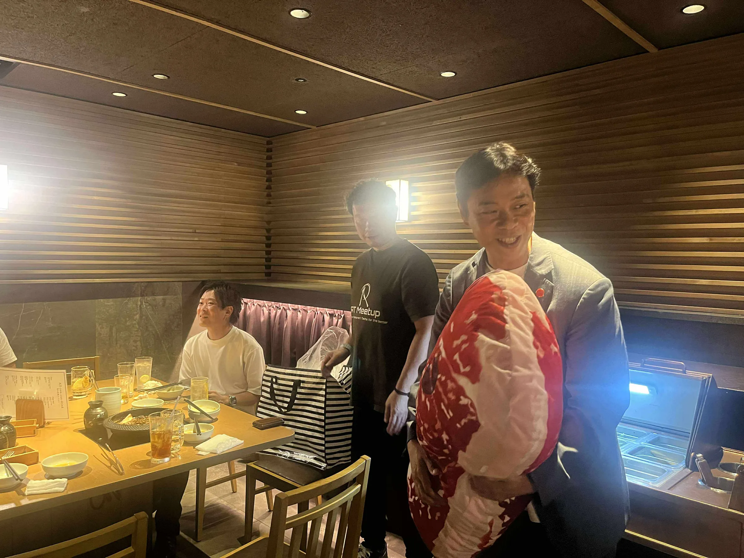 店の個室で、霜降り肉の形のクッションを抱えて笑う参加者