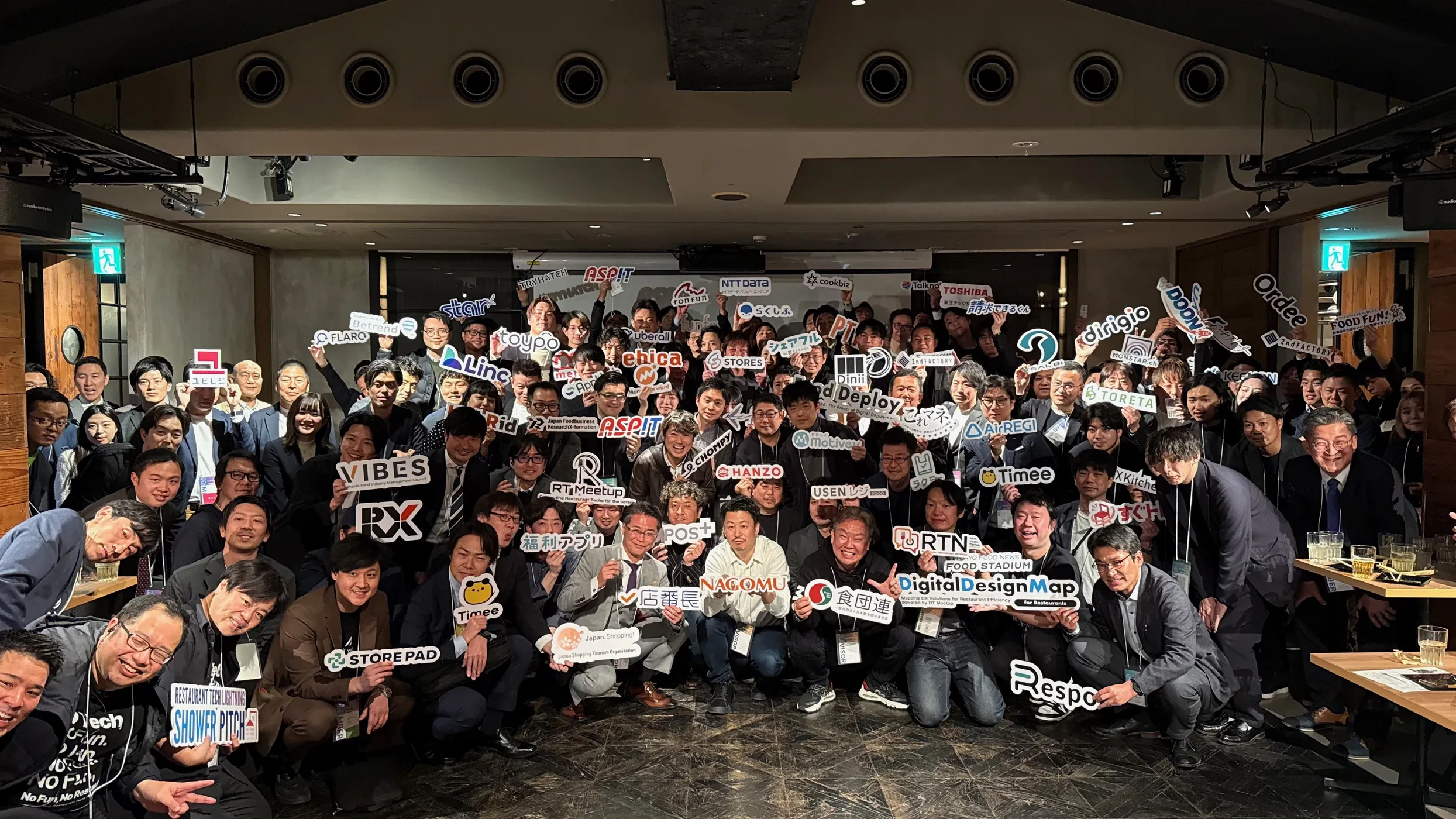 飲食革命の会場で、会員企業のロゴの札を持って集合写真におさまる参加者
