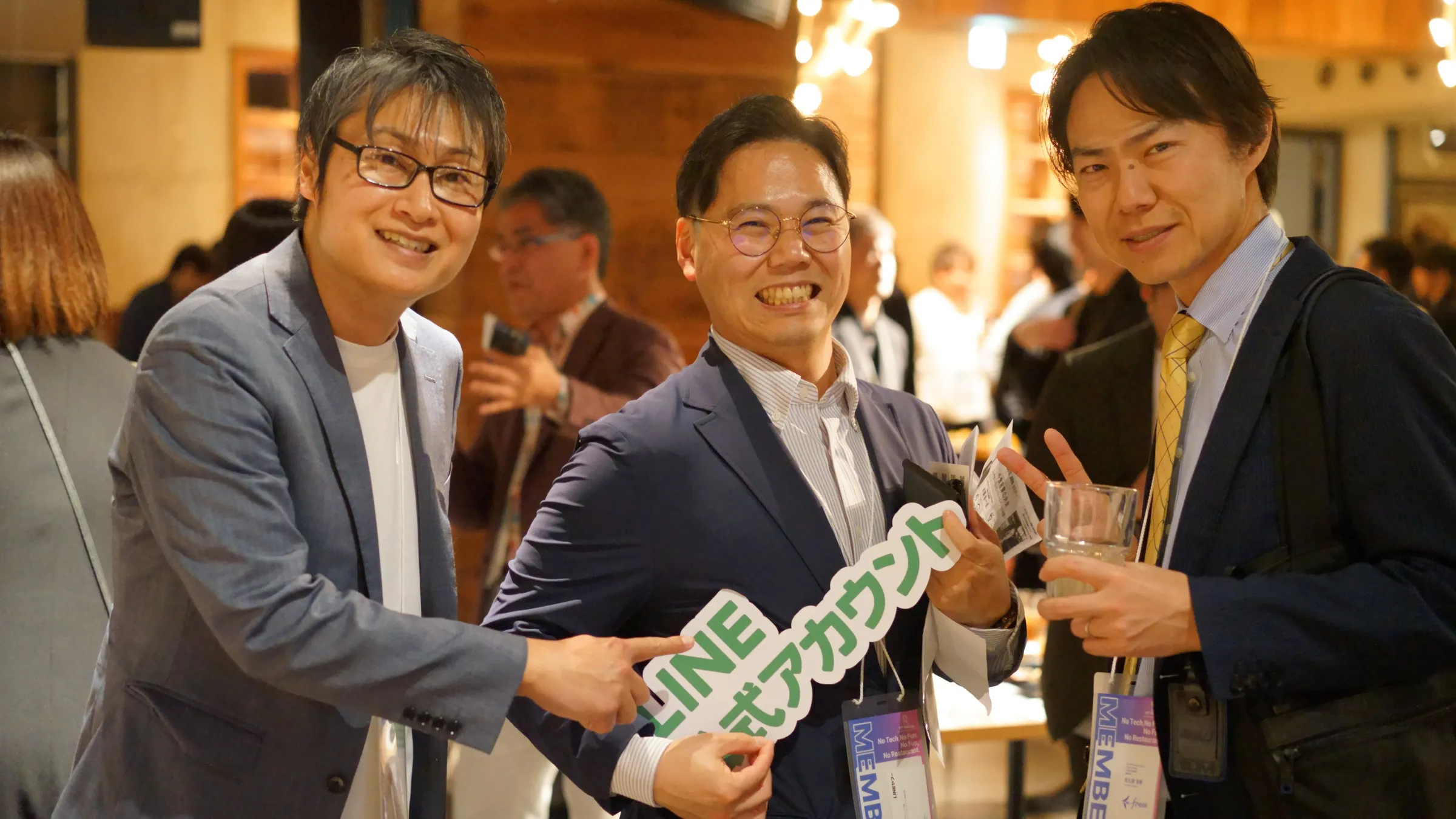 2025年3月の総会・懇親会で、サービスの札を持って並ぶ3人