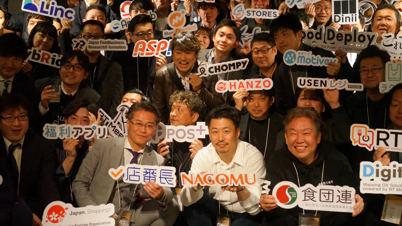 2025年3月の総会・懇親会で、会員企業のサービスのロゴの札を掲げる参加者